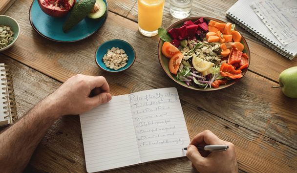Man making list of healthy food on wooden table - Foto, afbeelding