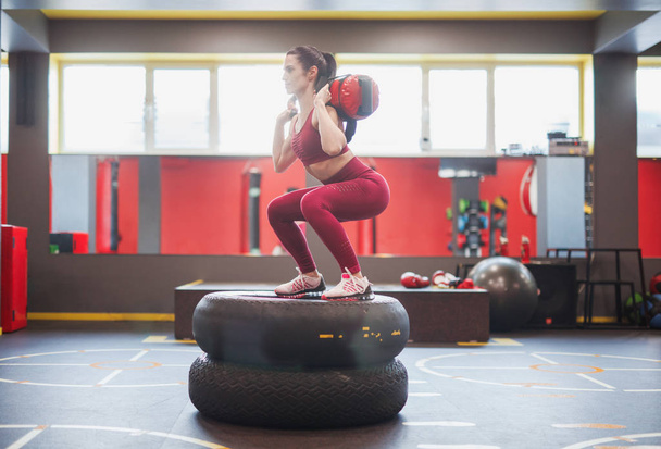 Sportswoman squatting with bag on tyres - Photo, Image