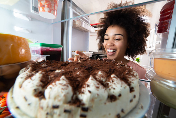 Giovane donna mangiare fetta di torta dal frigorifero
 - Foto, immagini