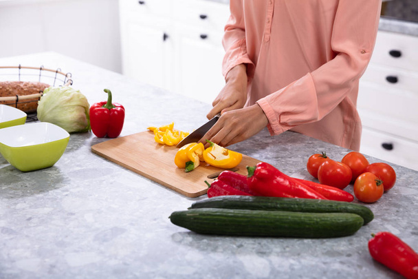 Woman Chopping Bell Pepper On Chopping Board With Knife Over The Kitchen Counter - Zdjęcie, obraz
