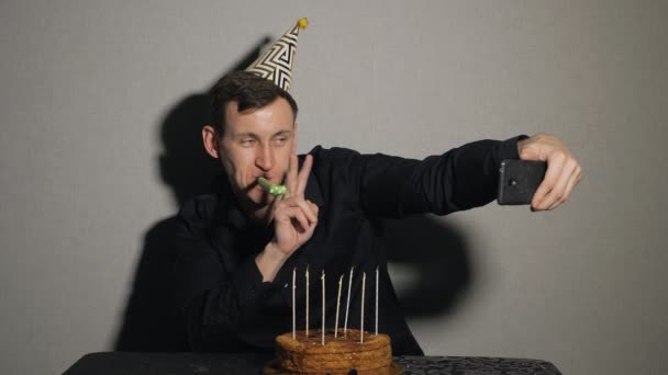 jonge man met chocolade cake en een kaarsen met partij blowers en neemt selfie - Video