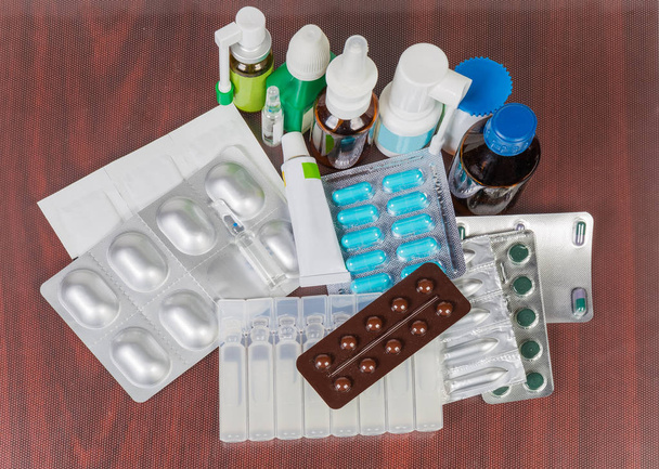 Várias pílulas, pomada, sprays, medicamentos em pó e líquidos em diferentes tipos de embalagem em uma mesa
 - Foto, Imagem