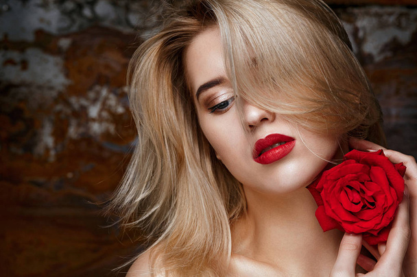 Beauty portrait of fashionable blonde model with naked shoulders posing at studio with red rose. Space for text - Zdjęcie, obraz