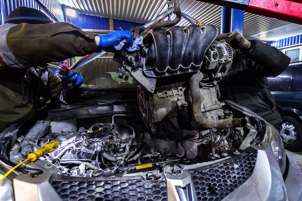 Close-up van de installatie van de motor op een oude auto met een pneumatische handmatige kraan in de auto reparatiewerkplaats. Het werk van auto mechanica te verwijderen van de motor - Foto, afbeelding