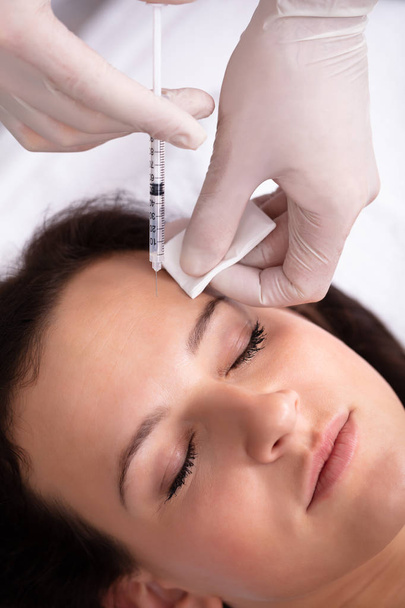審美的な治療を受けている女性の額に注射を与える美容師 - 写真・画像