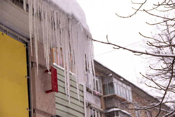 Large iced icicles hanging from the roof of the house , a danger to passersby - Photo, Image
