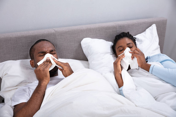 Sick African Young Couple Lying On Bed Blowing Their Nose In Bedroom - Foto, Imagem
