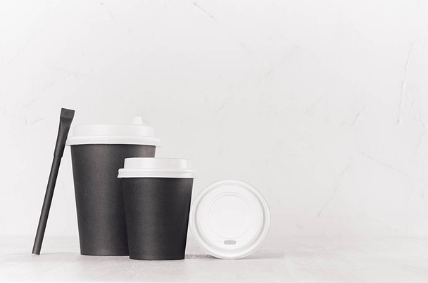 Coffee mockup - group black paper cups, blank white cap and sugar bag on white wood table with copy space, coffee shop interior. Modern elegant concept for branding identity, advertising, design. - Foto, Imagem