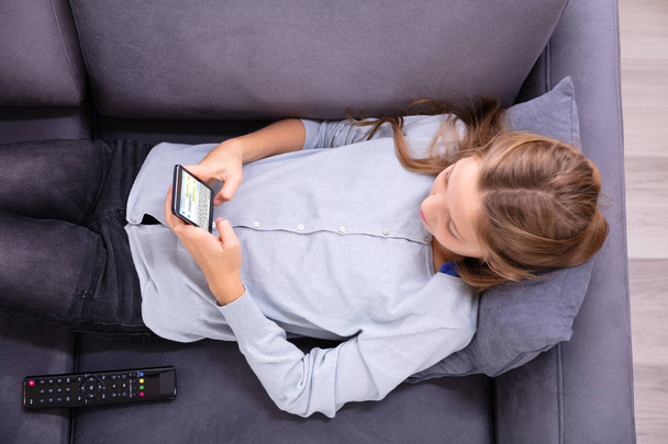 High Angle View Of A Girl Relaxing On Sofa Typing Text Message On Cellphone - Φωτογραφία, εικόνα