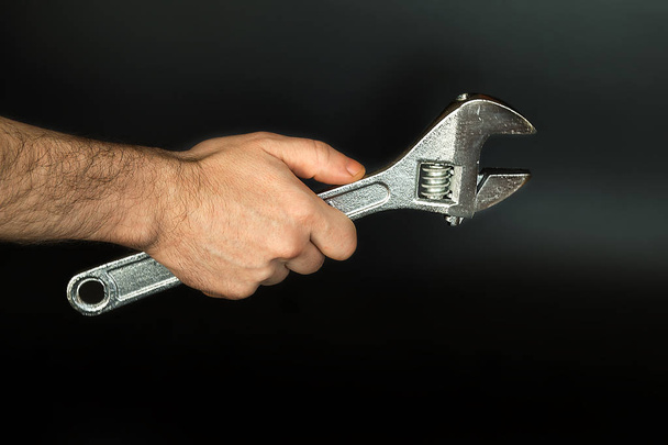Male hand holding a metal adjustable wrench on a black background. Plumber and locksmith tools and works. Selective focus. - Foto, Imagem