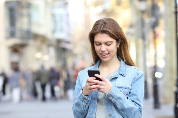 Portrait of a happy teen texting messages on a smart phone in the street - Foto, afbeelding