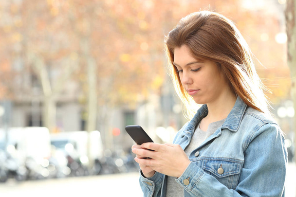Adolescente sérieuse bavardant sur le téléphone intelligent marchant dans la rue
 - Photo, image