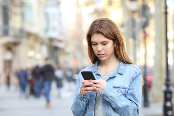 Serious teenage girl  texting messages on smart phone walking in the street - Foto, Imagem