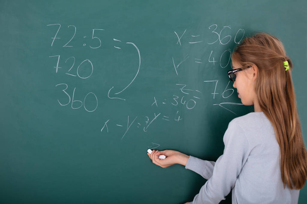 Rear View Of A Girl Wearing Eyeglasses Solving Mathematics On Chalkboard - Foto, Bild
