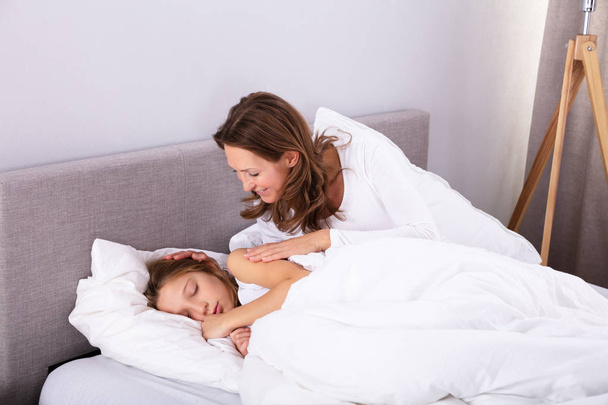 Mature Woman Waking Up Her Daughter Sleeping On Bed In Bedroom - Foto, immagini