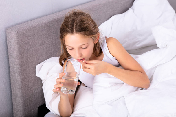 Girl Lying On Bed Taking Medicine With Glass Of Water - Foto, Bild