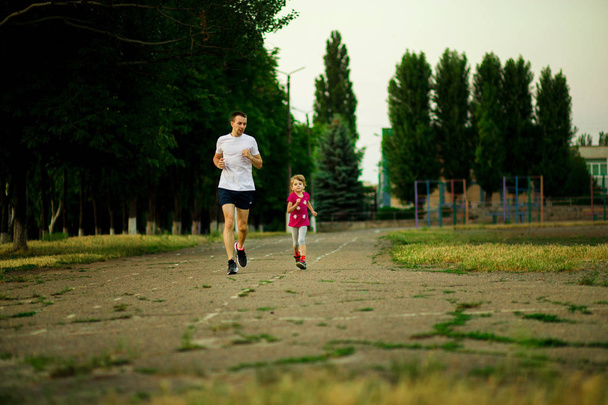 Nuori urheilullinen isä ja pieni tytär juoksevat stadionilla auringonlaskun aikaan. Terveellinen elämäntapa
 - Valokuva, kuva