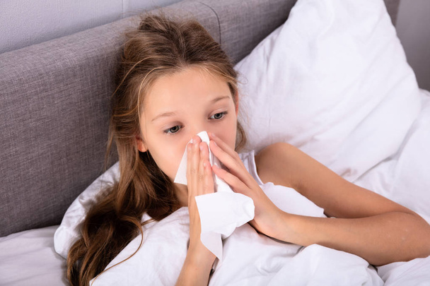 Dívka trpí studené foukání jí nos kapesníkem na posteli - Fotografie, Obrázek