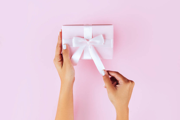 Woman hands holding present box with pink bow on pastel pink bac - Foto, Imagen