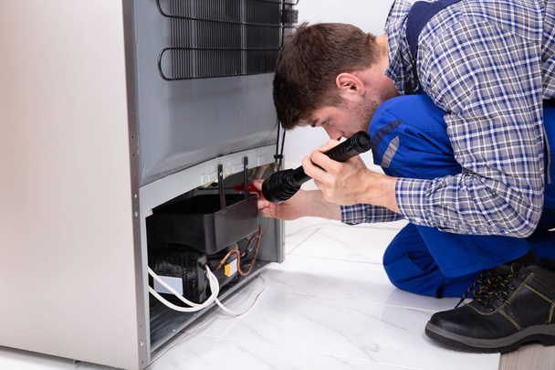Close-up Of Handyman Checking Refrigerator With Flashlight At Home - Valokuva, kuva