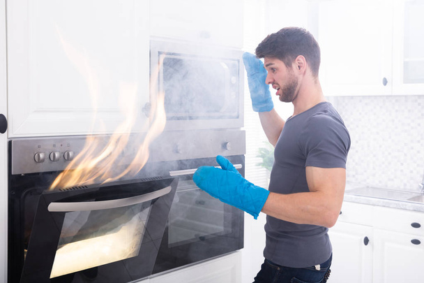 Afraid Young Man Looking At Fire Coming Out From Oven In Kitchen - Photo, Image