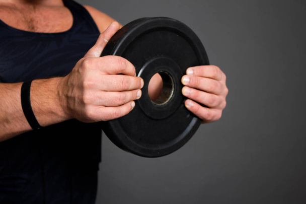 Izmos fiatalember nehéz súlyzó tömege a kezével tartja a fekete háttér kemény edzés az edzőteremben - Fotó, kép