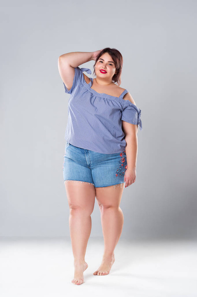 Plus size fashion model in jean shorts, fat woman on gray studio background, overweight female body - Fotoğraf, Görsel