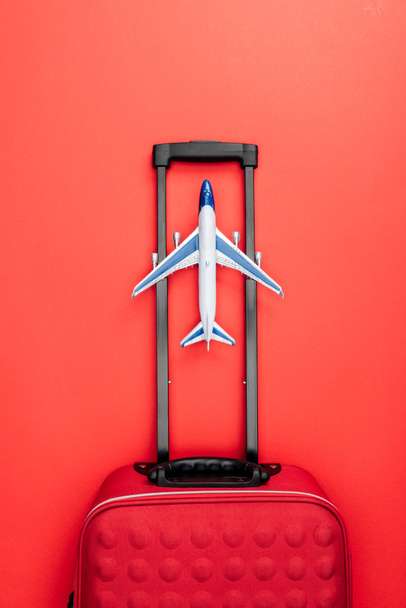 kolu ve oyuncak uçak ile seyahat çantası üstten görünüm kırmızı zemin üzerine  - Fotoğraf, Görsel