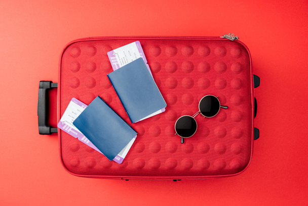 vista superior de la bolsa de viaje, pasaportes, billetes de avión y gafas de sol sobre fondo rojo
  - Foto, Imagen