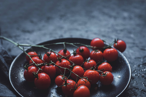 Branch of ripe cherry tomatoes on black plate, close up. With copy space - Φωτογραφία, εικόνα