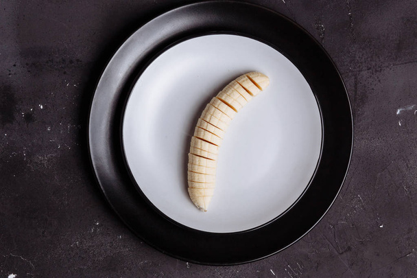 Closeup of sliced banana in a plate on a black wooden background on a table, top view, flat lay - Fotó, kép