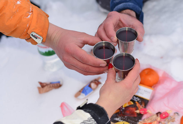 Ukraine, Osmoloda- January 13, 2019:  Tourists celebrate on a mountain peak in the Carpathians. Hands with cups of liquor on the background of a snack on the snow. - Fotó, kép