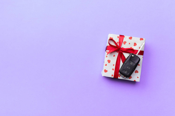 Llave del coche en caja de regalo de papel con lazo de cinta roja y corazón sobre fondo de mesa violeta. Vacaciones presente concepto de vista superior
. - Foto, imagen