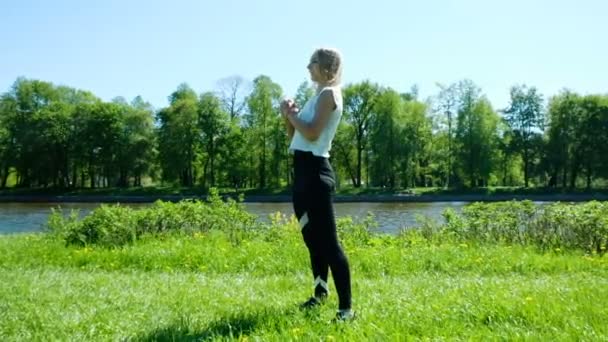 Sportieve meisje houdt warming-up in de natuur - sprongen en pompen benen spieren, slow-motion - Video