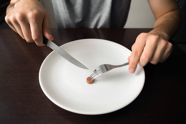 Здоровое питание, бедность, экономия денег: монеты на белой тарелке в столовой. Нож и вилка в руках
 - Фото, изображение