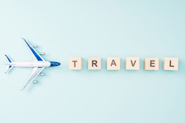 top view of toy plane and wooden cubes with travel lettering on blue background - Foto, afbeelding