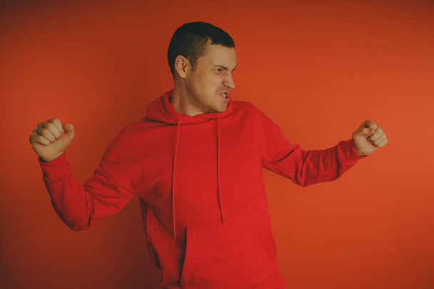 Crazy and charismatic guy posing on an orange background. A man in a red tracksuit. - Photo, image