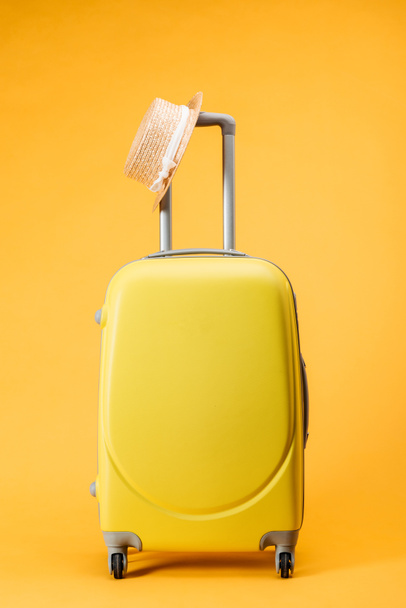 travel bag with wheels and straw hat on yellow background - Фото, зображення