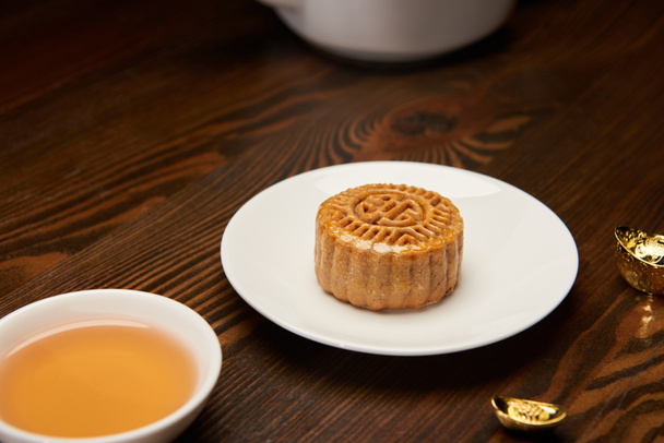 selective focus of mooncake with tea cup and gold ingots on wooden table - Photo, Image