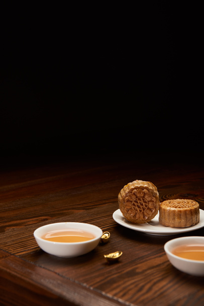 traditional mooncakes with tea cups and gold ingots isolated on black with copy space - Photo, Image