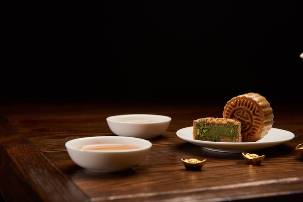 gâteaux chinois traditionnels, tasses de thé et lingots d'or isolés sur noir
 - Photo, image
