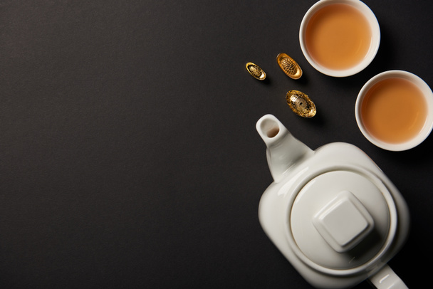 pohled shora zlatých ingotů, čajové konvice a šálky izolované na černém pozadí s kopií prostor - Fotografie, Obrázek