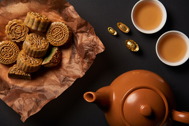 top view of mooncakes, tea pot and gold ingots isolated on black - Fotó, kép