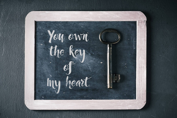 a key on a chalkboard where you can read the text you own the key of my heart, on a dark background - Фото, зображення