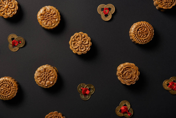 вид сверху на традиционные лунные кексы и монеты фэн-шуй, изолированные на черном
 - Фото, изображение