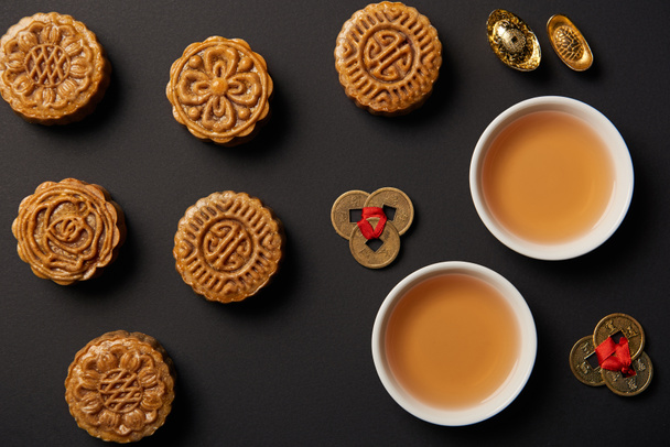 вид сверху на традиционные лунные пирожные, чашки чая и монеты фэн-шуй, изолированные на черном
 - Фото, изображение