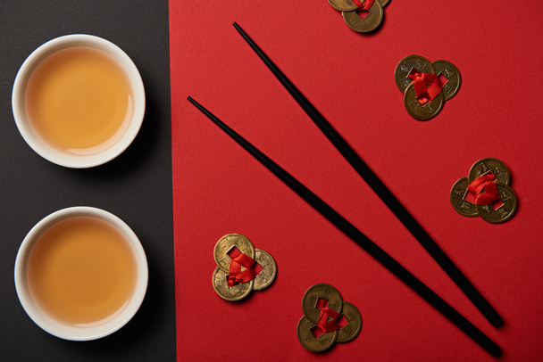 top view of tea cups, feng shui coins and chopsticks on red and black background  - Photo, Image