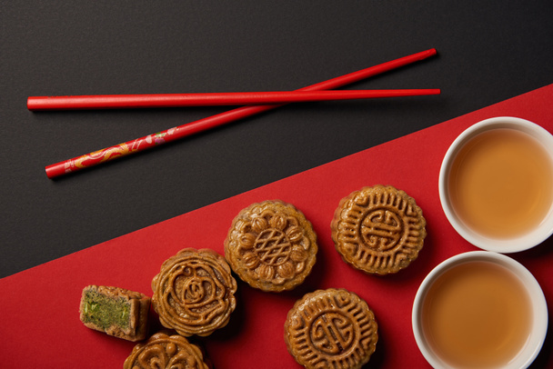 top view of traditional chinese mooncakes with chopsticks on red and black background - Foto, afbeelding
