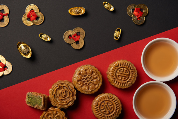 top view of mooncakes, feng shui coins and cups with tea on red and black background - Photo, Image