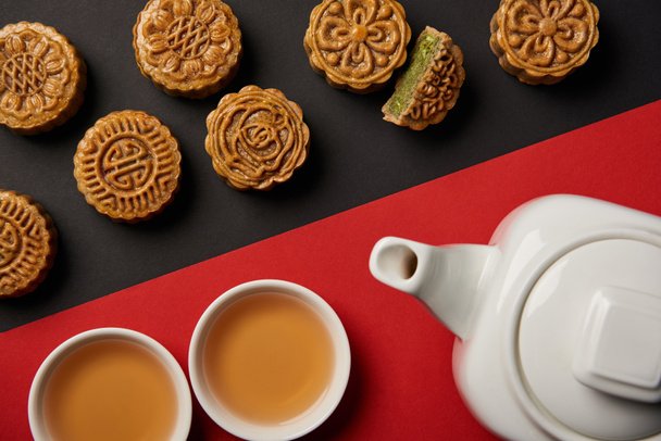 top view of mooncakes, tea pot and cups on red and black background  - Foto, Imagem